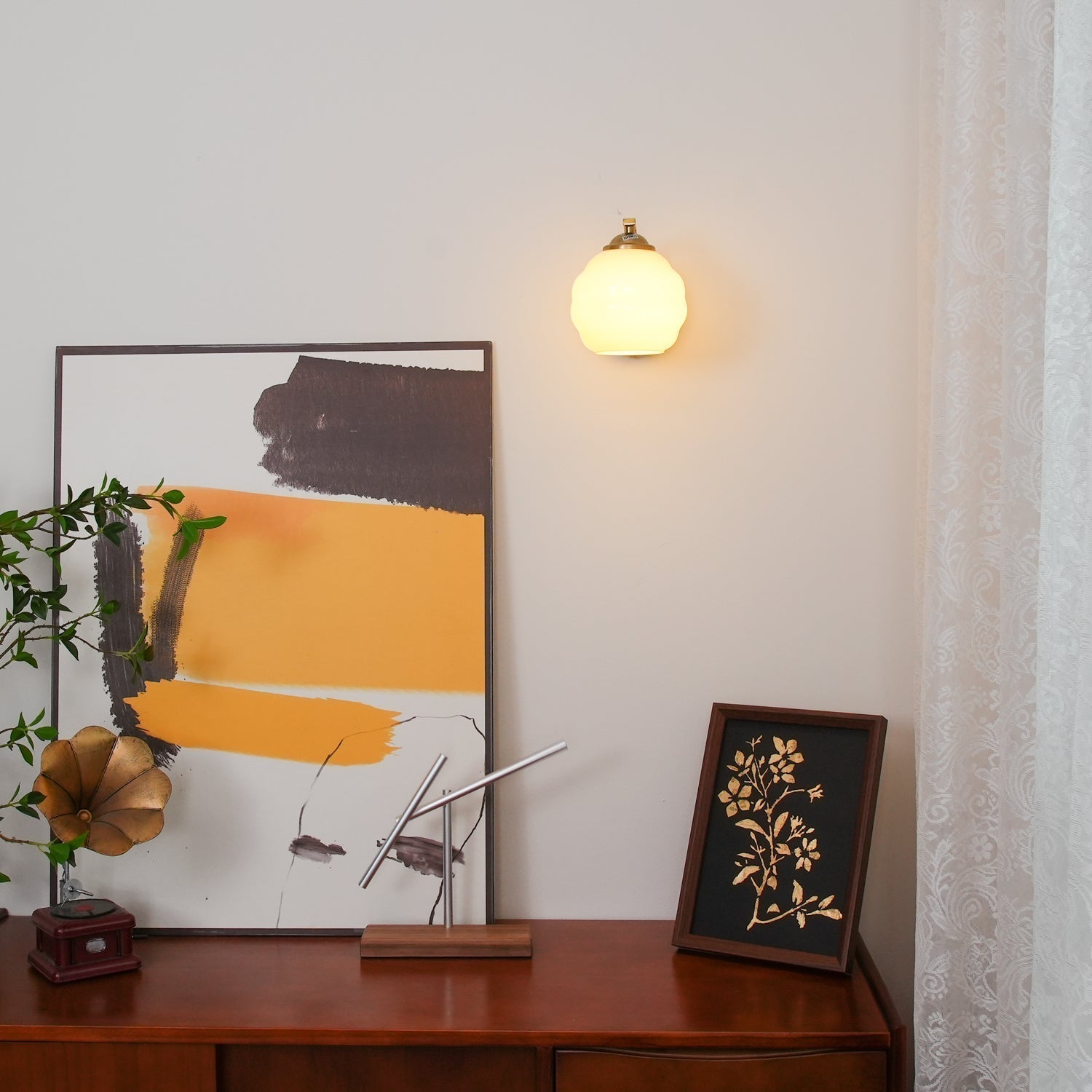 Lit Clérachic gold wall sconce, its warm glass lantern glowing above a dark wood sideboard and abstract art.