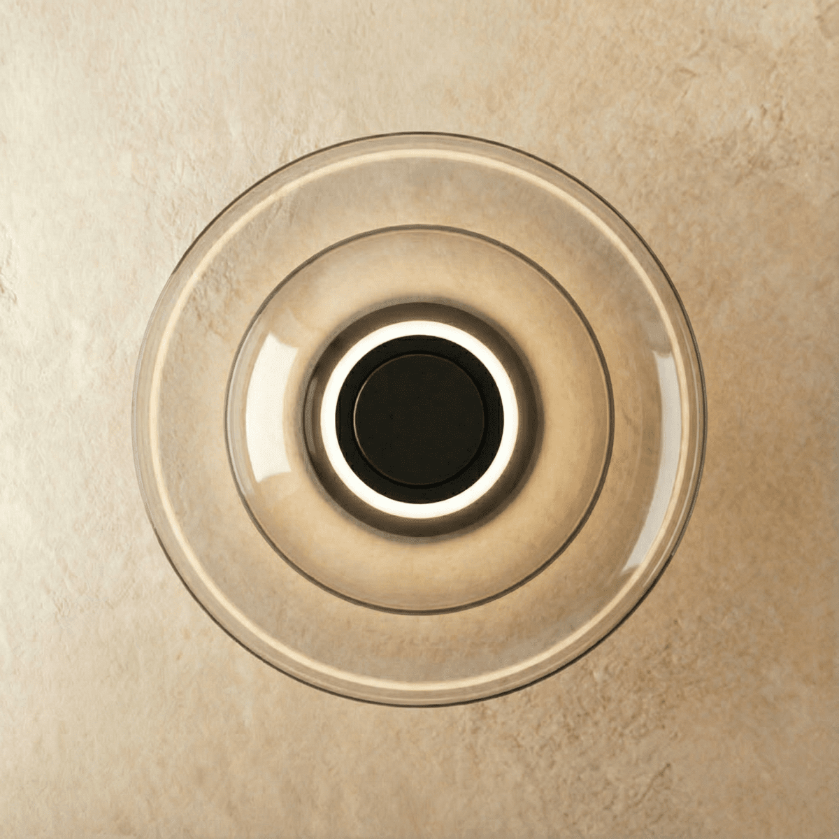 Clérachic round wall light of layered smoky grey glass discs with a glowing ring around a black centre, on limewash.