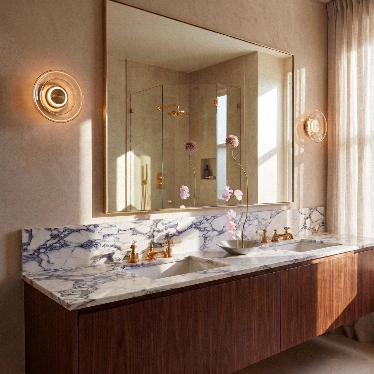 Clérachic pair of round amber glass wall lights flanking a large gold-framed mirror above a marble-topped counter.