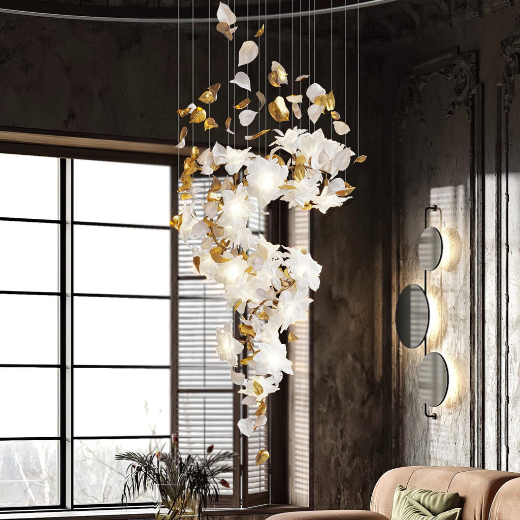 In a room with tall paned windows and dark panelled walls, a Clérachic chandelier trails white petals and brass leaves from the ceiling.