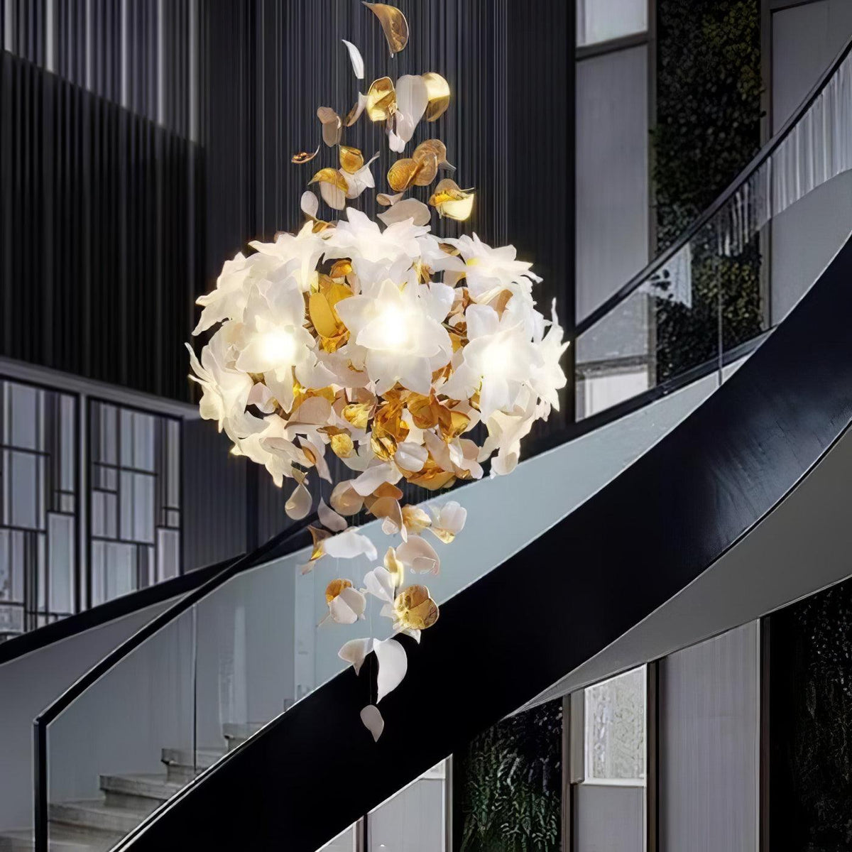 The rounded white petal cluster of this Clérachic chandelier glows over a black curved stair rail, brass leaves falling beneath it.