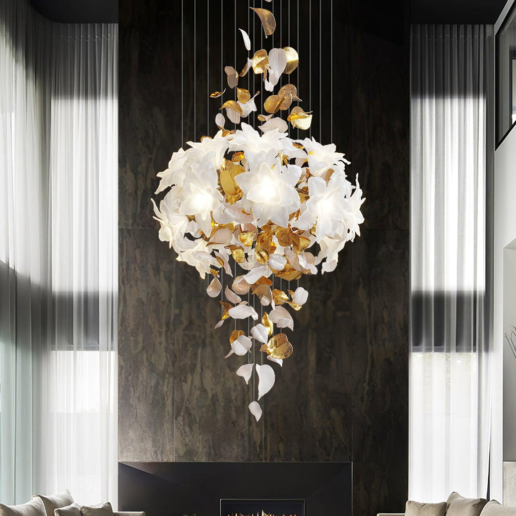 Against a dark stone wall between sheer curtains, a Clérachic chandelier shows a full round cluster of white petals above hanging leaves.