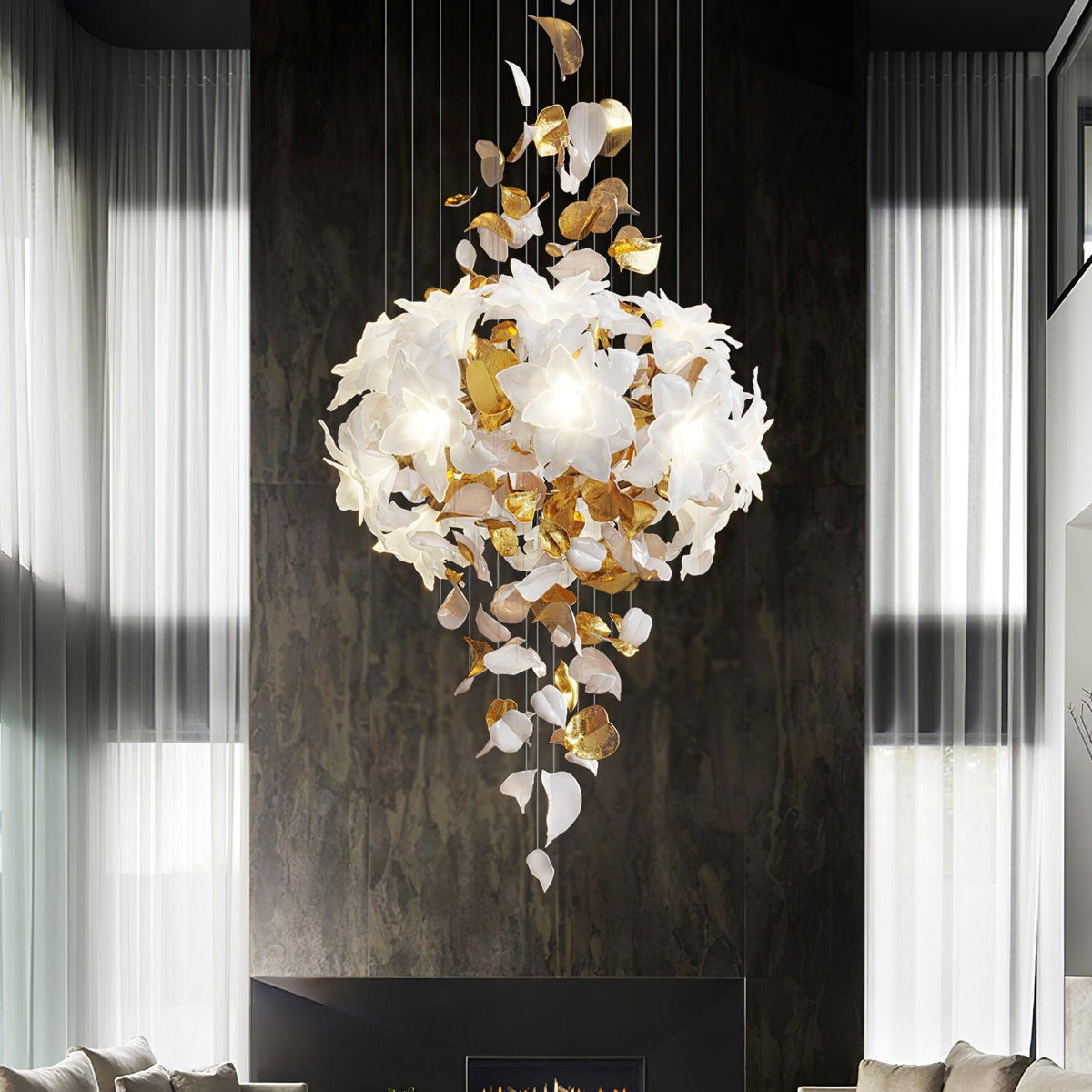 Against a dark stone wall between sheer curtains, a Clérachic chandelier shows a full round cluster of white petals above hanging leaves.