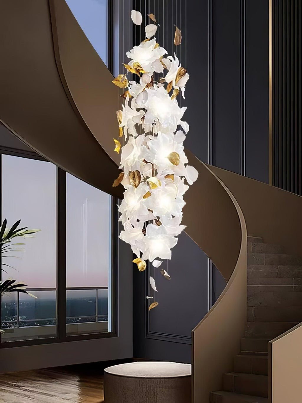 A narrow column of lit white petals with brass accents, this Clérachic chandelier hangs in a curved stairwell beside a tall window.