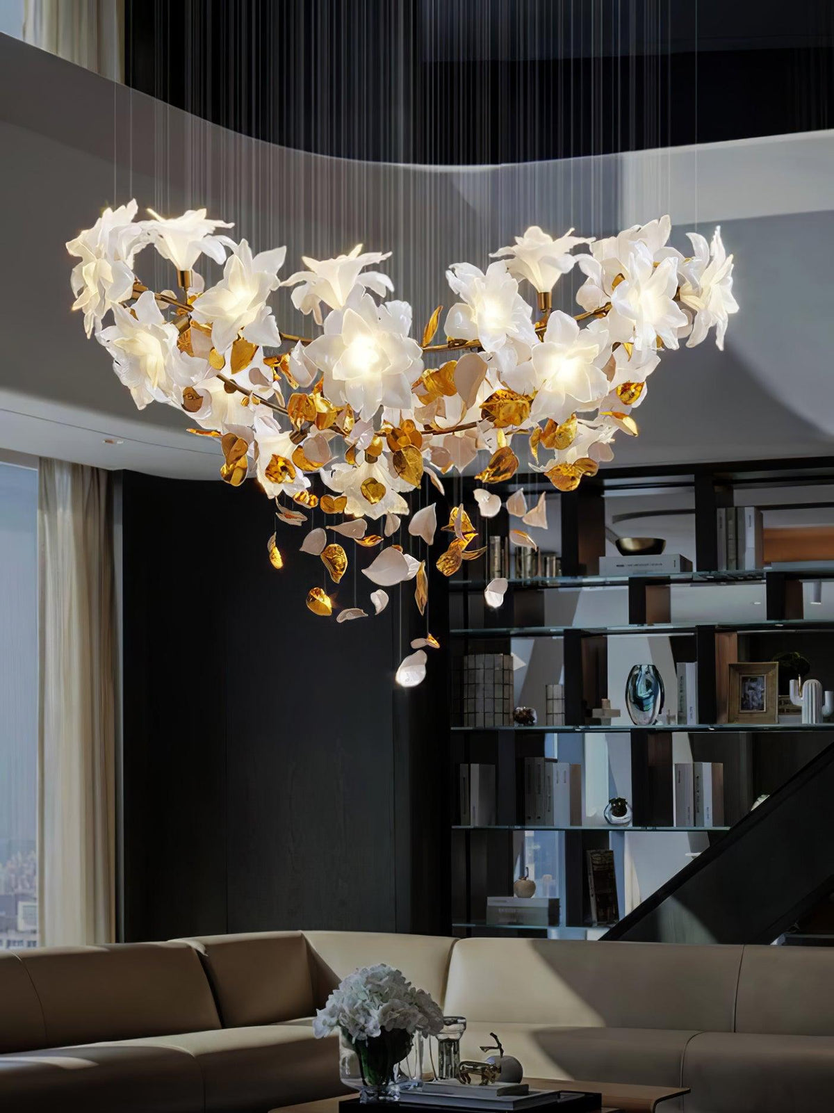 A wide Clérachic chandelier with white petal flowers on a brass ring hangs above a sofa and a dark glass-fronted shelf.