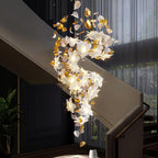 Hung down a stairwell with a dark wall and sheer curtains behind, this Clérachic chandelier glows in a long, twisting spiral of petals.