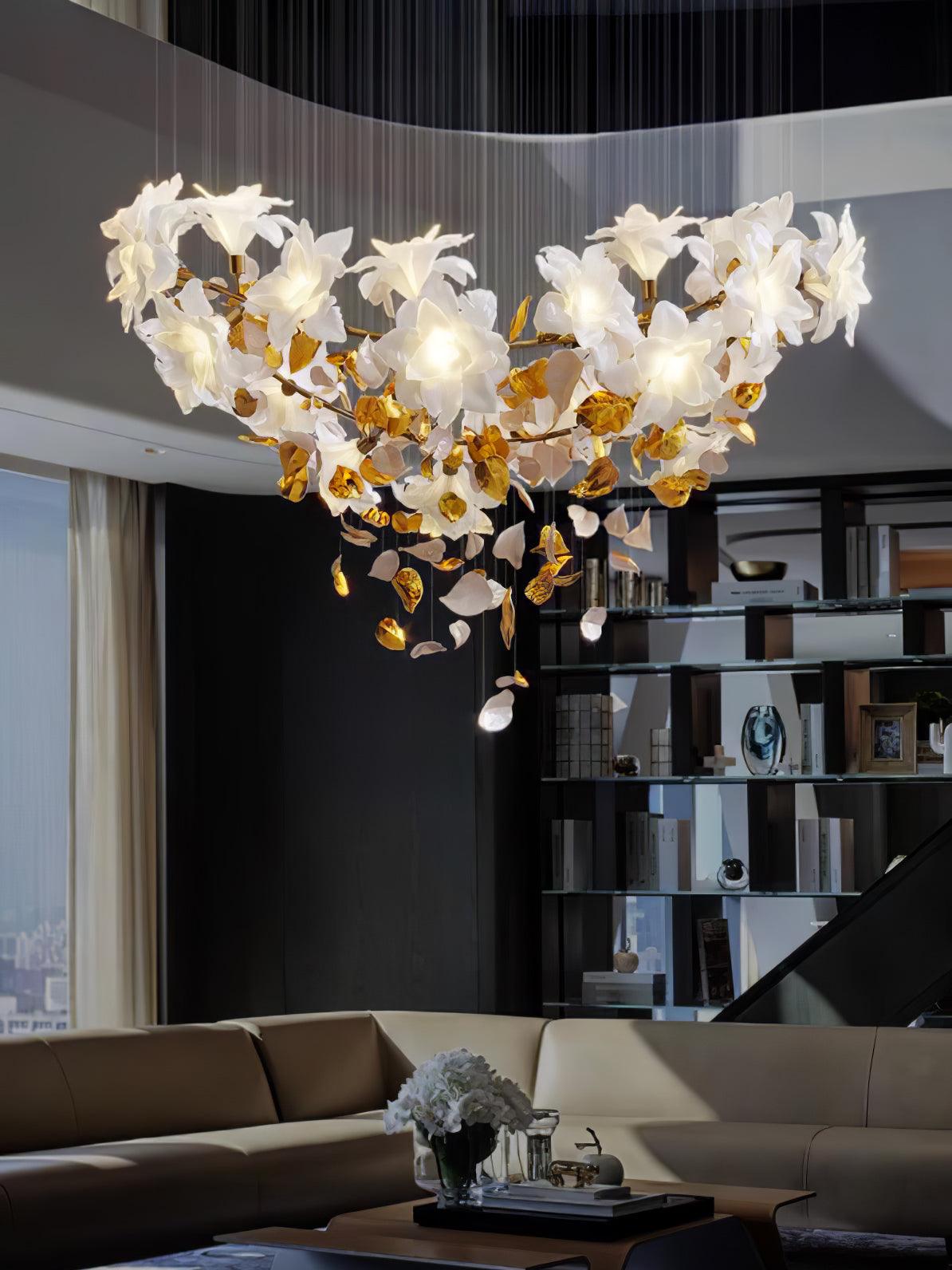 Wide and low over a sofa and tall bookcase, this Clérachic chandelier of white petals and brass leaves is shown in a high-ceilinged lounge.