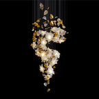 On a black backdrop, this Clérachic chandelier shows its lit white petals and brass leaves twisting down from a curtain of fine cords.