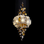 On a black backdrop, a lit Clérachic chandelier shows a full round bloom of white petals with brass leaves hanging below it.