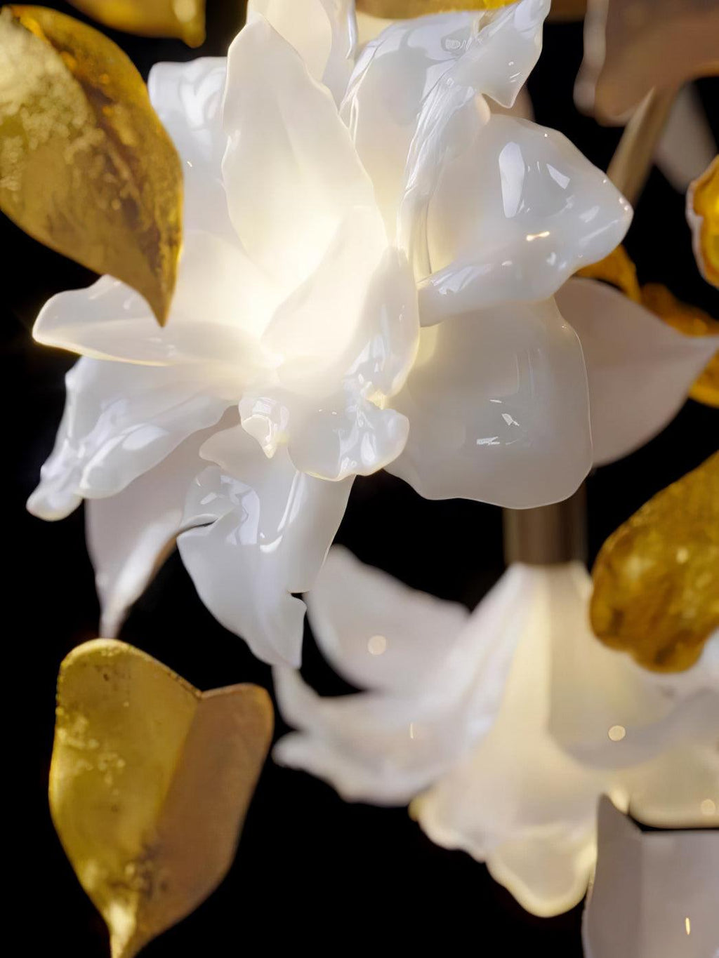 Close view of the glazed white petal flowers and brass leaves on this Clérachic chandelier, lit from within against black.