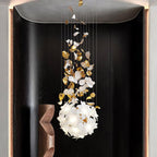 Framed in a dark recess beside a walnut sculpture, this Clérachic chandelier ends in a round ball of white petals with brass leaves above.