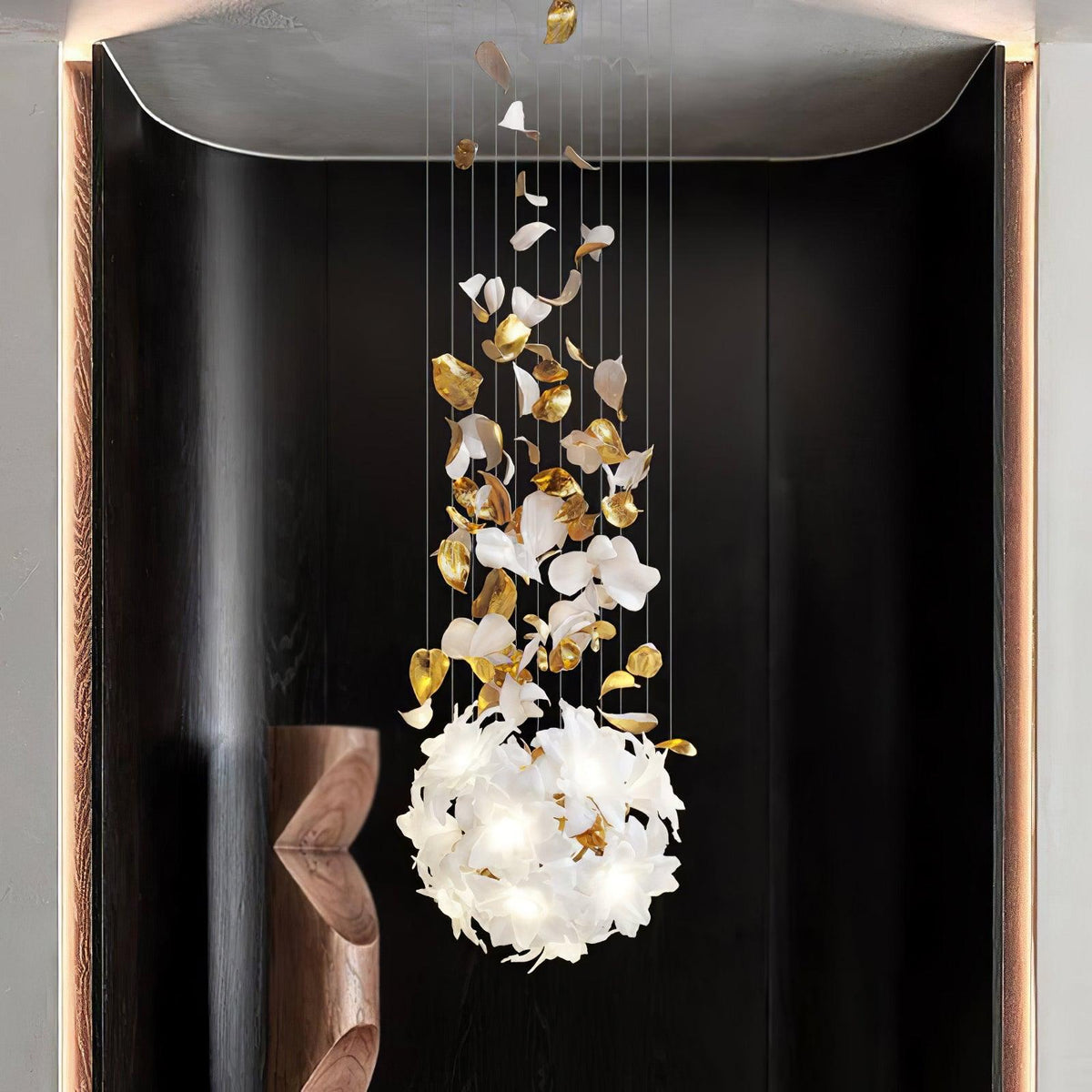Framed in a dark recess beside a walnut sculpture, this Clérachic chandelier ends in a round ball of white petals with brass leaves above.