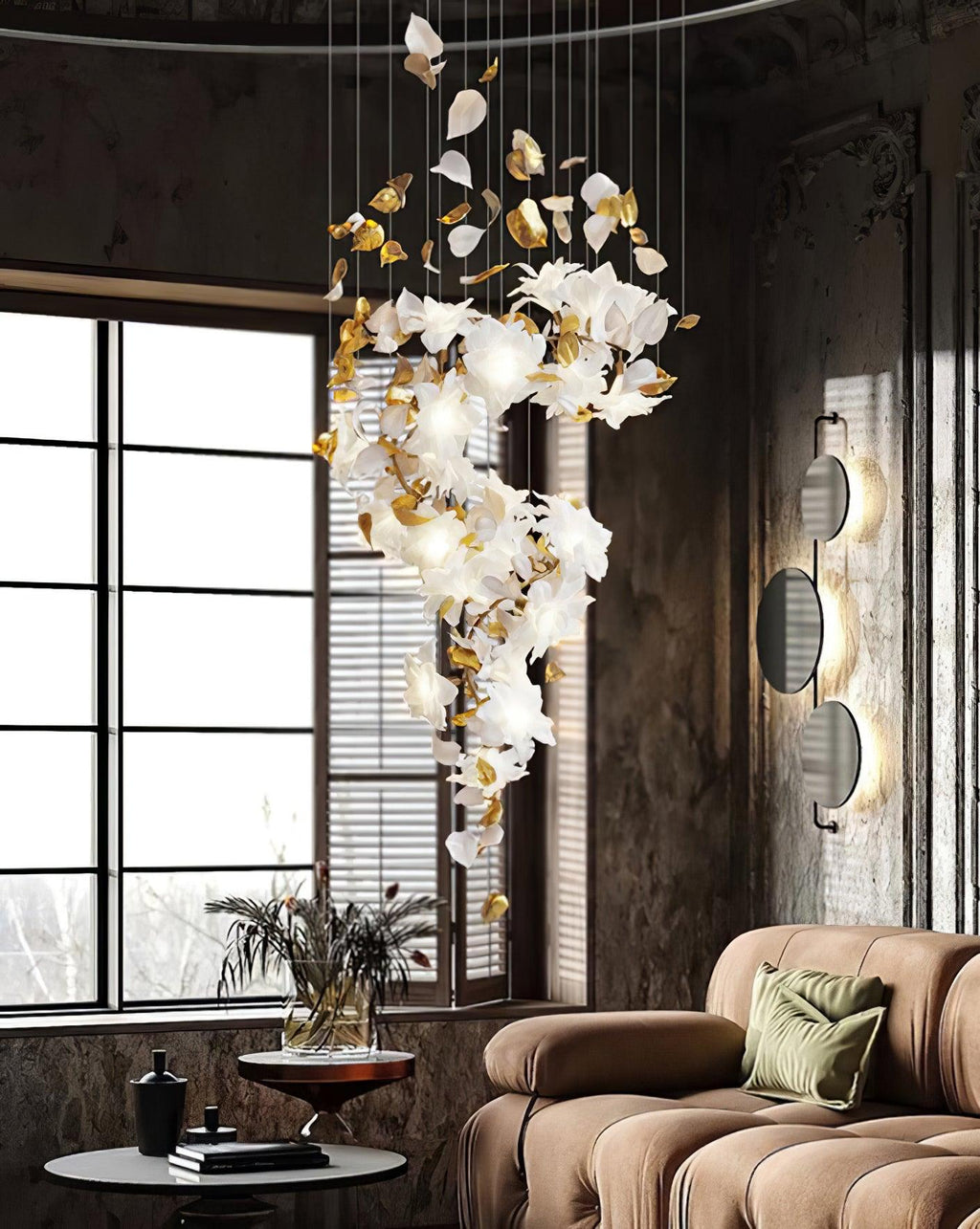 By a tall paned window and a tan sofa, this Clérachic chandelier trails an S of white petals and gold leaves against a rough dark wall.