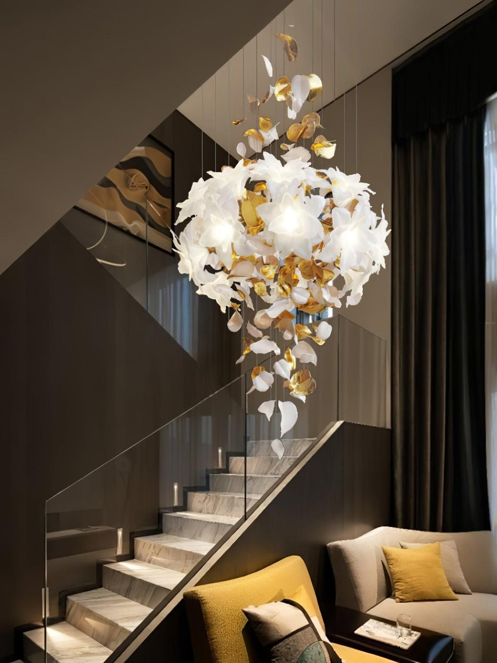 Over a glass-sided staircase and a mustard armchair, this Clérachic chandelier shows a round cluster of petals and trailing brass leaves.