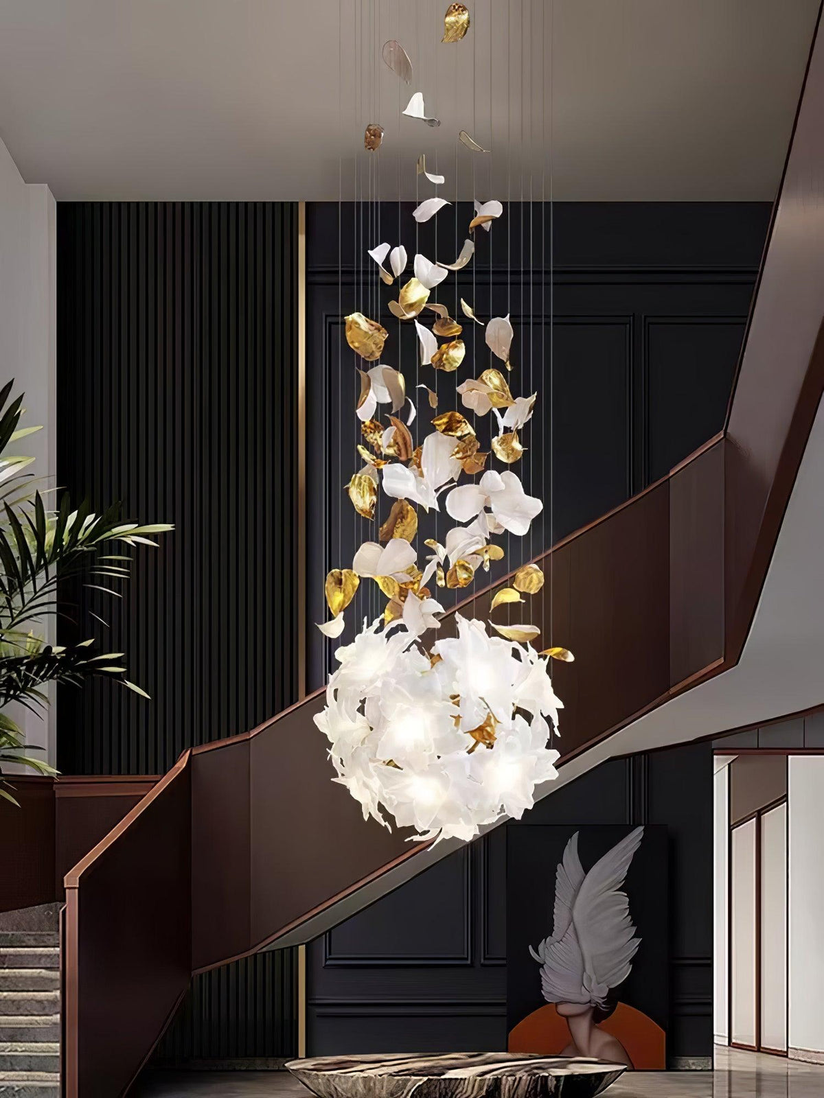 Beside a copper-brown stair rail and a feathered sculpture, this Clérachic chandelier ends in a round, lit cluster of white petals.