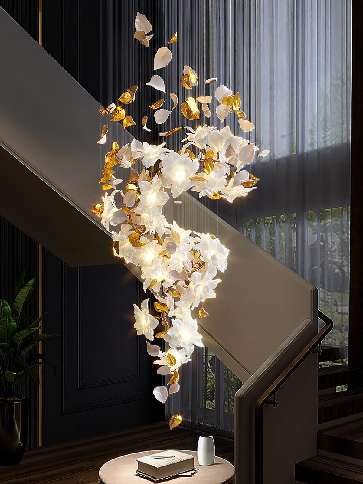 Above a round side table with a book and a vase, this Clérachic chandelier curves down a dark stairwell in lit white petals and brass.