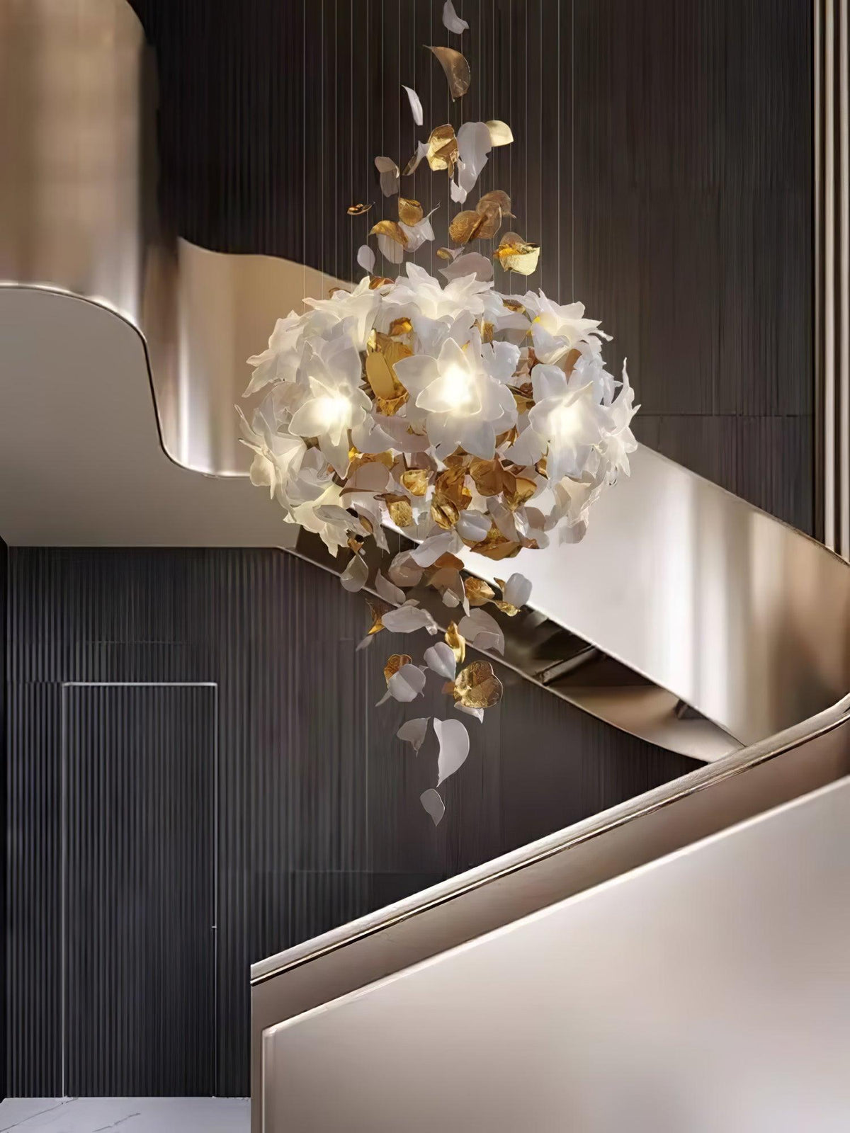 Next to a sweeping pale curved balustrade, a Clérachic chandelier of white petals and brass leaves hangs in a rounded, lit cluster.