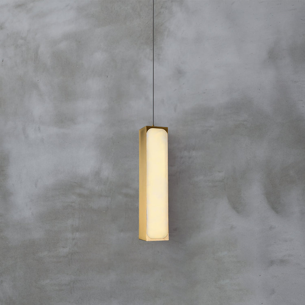 Clérachic Gleam pendant, a slim brass-framed alabaster column glowing softly against a raw concrete wall.