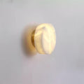 Angled view of the brass-backed Clérachic Glim Round Alabaster Wall Sconce, the lit stone disc standing just clear of the plaster.