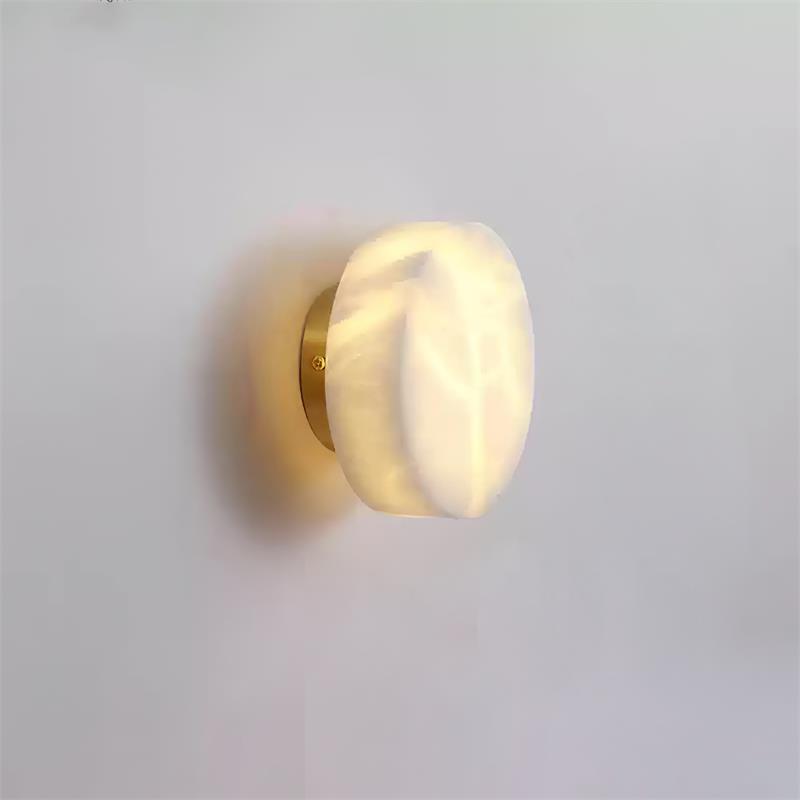 Angled view of the brass-backed Clérachic Glim Round Alabaster Wall Sconce, the lit stone disc standing just clear of the plaster.