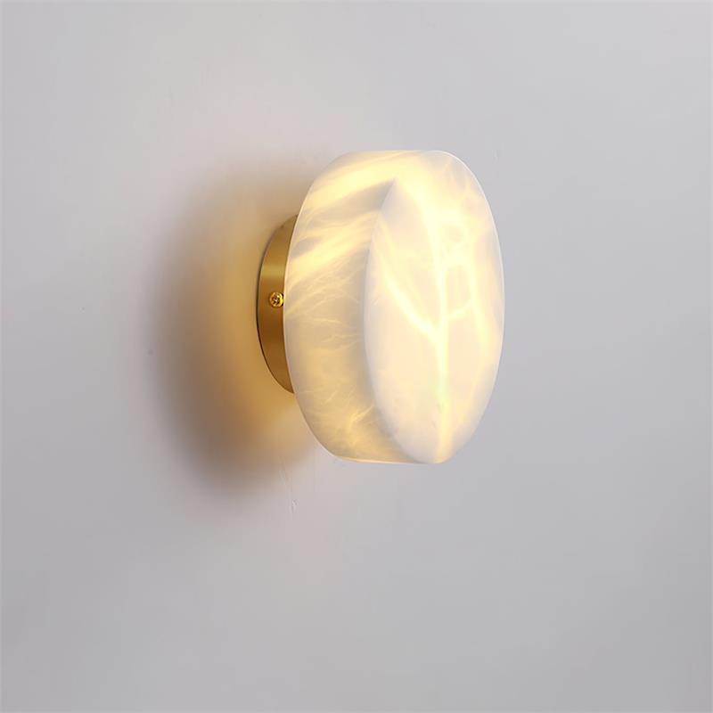 Wide brass-backed Clérachic Glim Round Alabaster Wall Sconce lit on a white wall, the veining spreading like frost across the face.