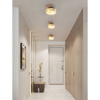 Three black-backed Clérachic Glim Round Alabaster Wall Sconces ceiling mounted in a line down a bright hallway toward the front door.