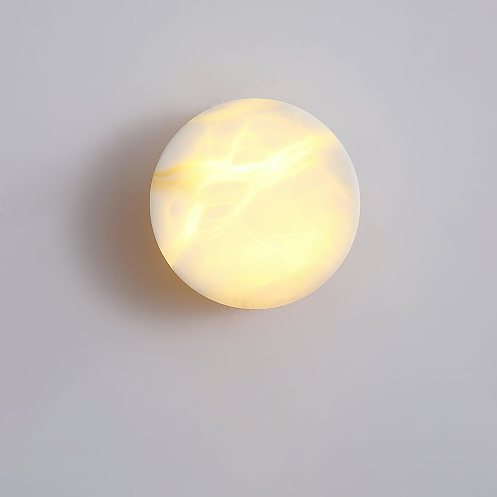 The Clérachic Glim Round Alabaster Wall Sconce seen face on, warm light picking out the amber veins running across the stone disc.