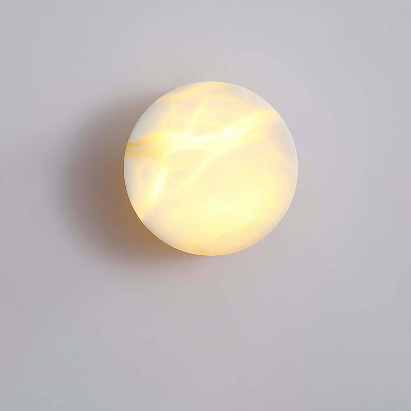 The Clérachic Glim Round Alabaster Wall Sconce seen face on, warm light picking out the amber veins running across the stone disc.