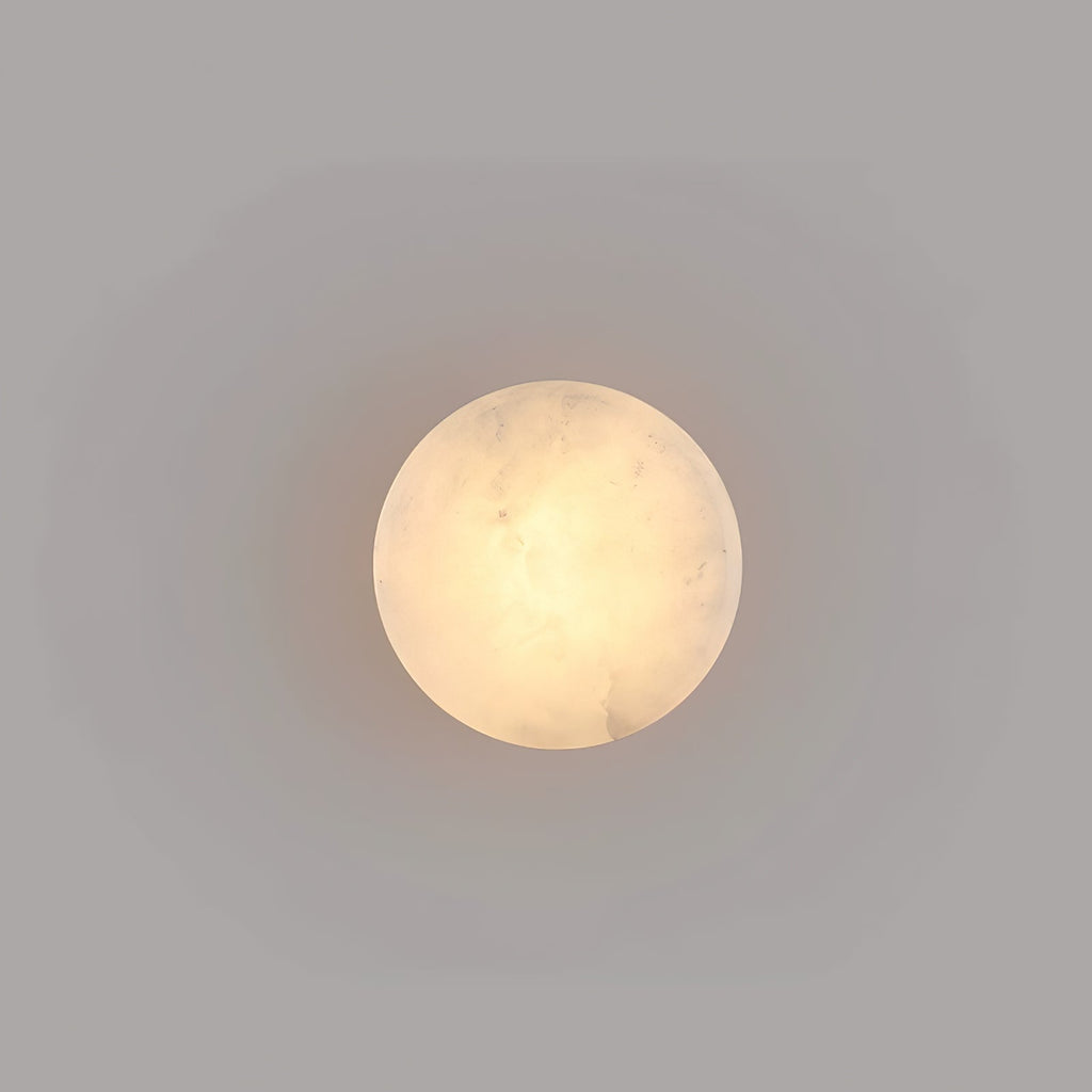 Face-on view of a smaller Clérachic Glim Round Alabaster Wall Sconce, its lit stone reading as a plain warm circle on a grey wall.