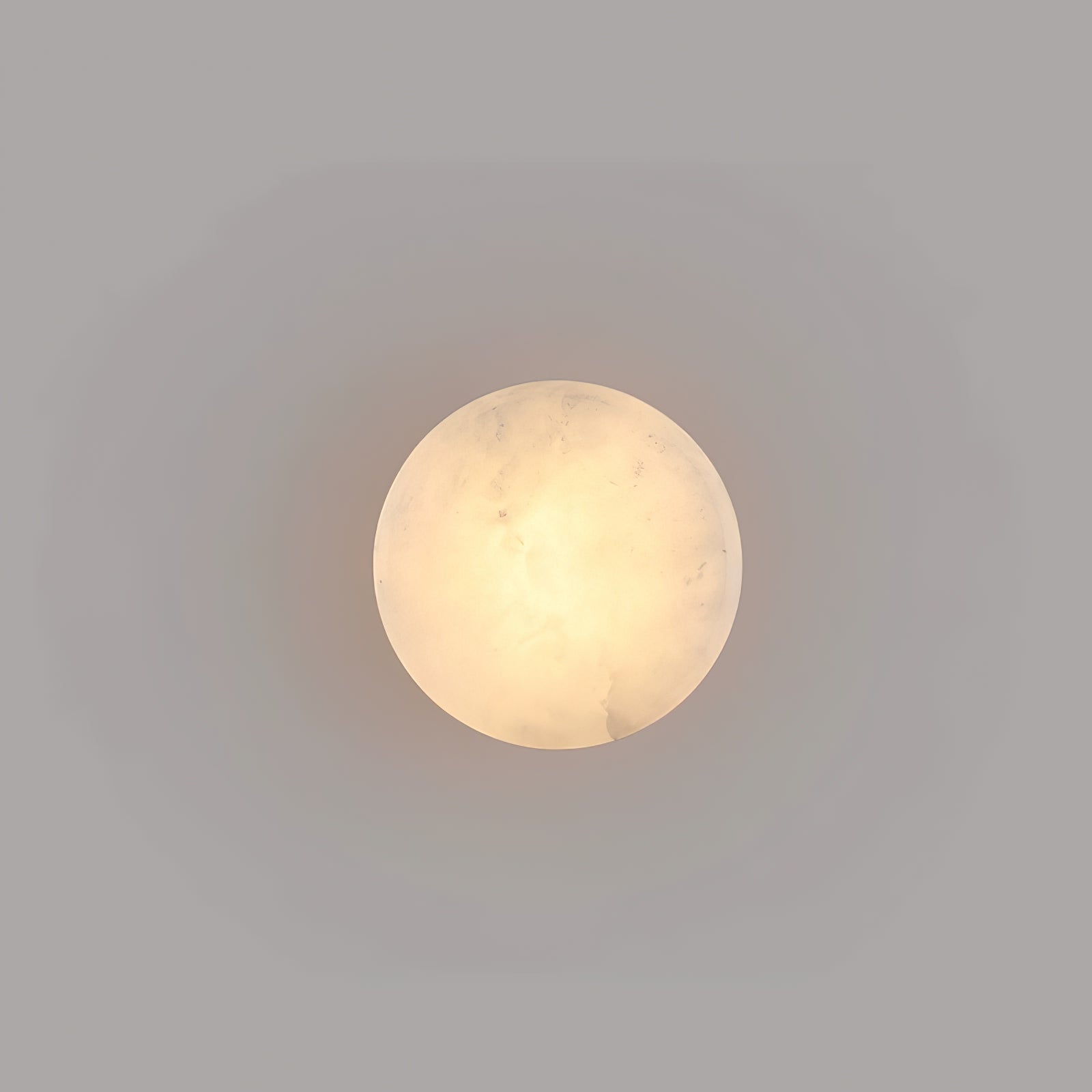 Face-on view of a smaller Clérachic Glim Round Alabaster Wall Sconce, its lit stone reading as a plain warm circle on a grey wall.