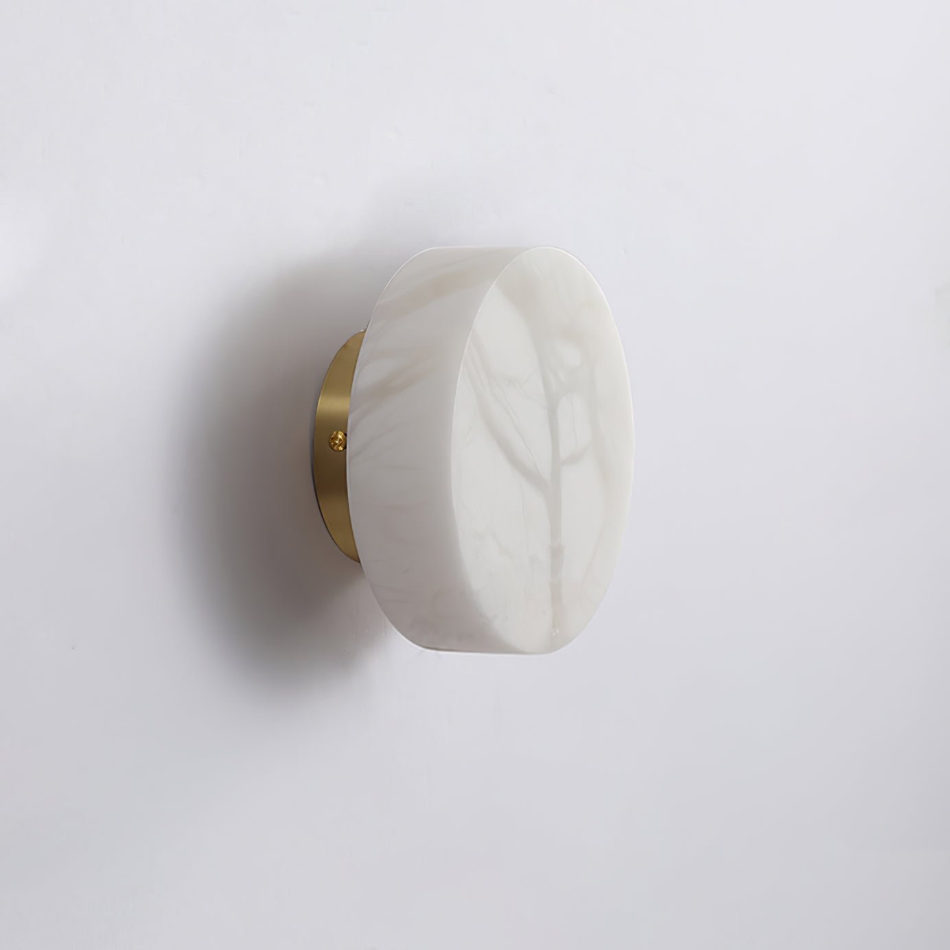 Unlit Clérachic Glim Round Alabaster Wall Sconce on a brass backplate, showing the cool grey markings in the natural alabaster.