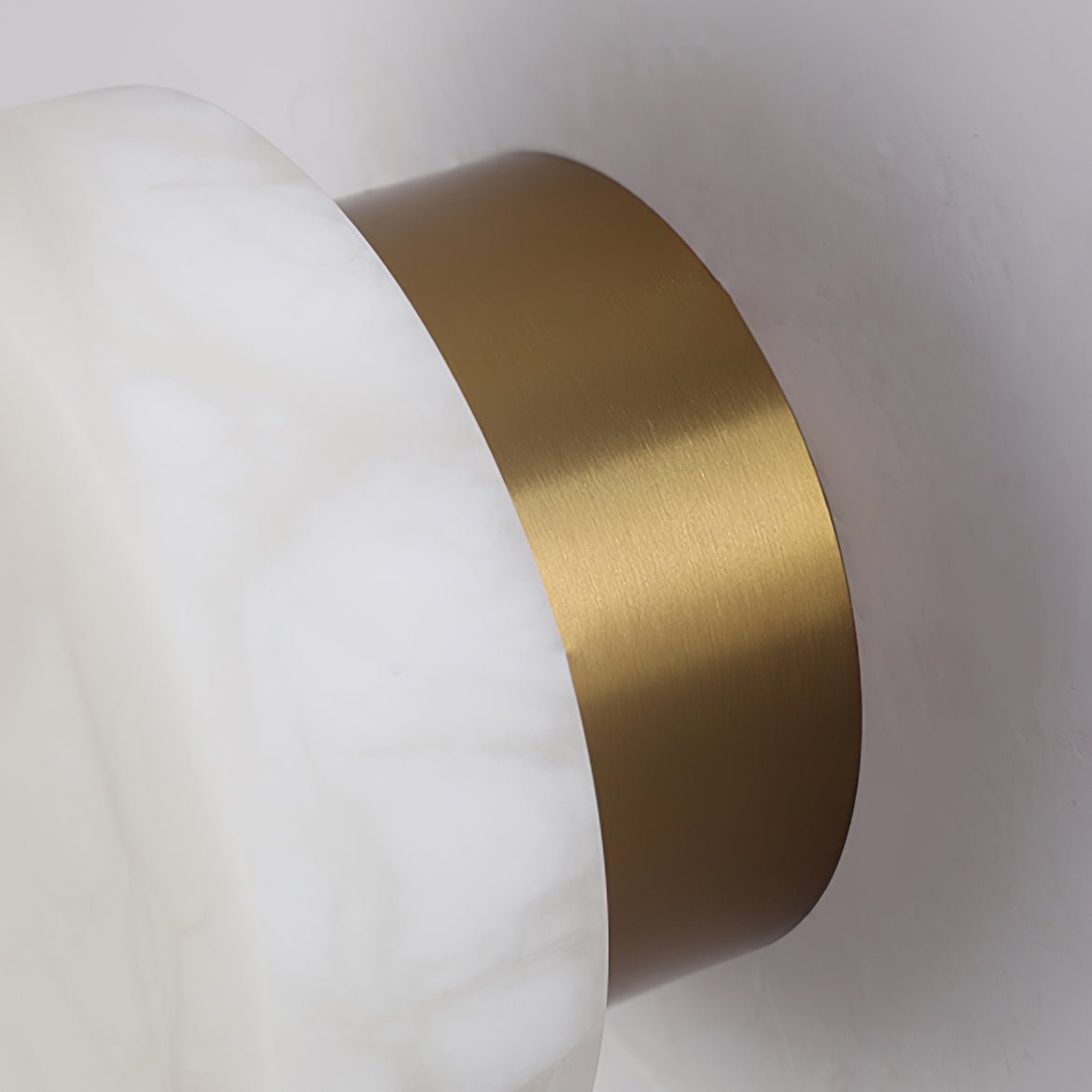 Close view of the brushed brass backplate on a Clérachic Glim Round Alabaster Wall Sconce, meeting the cut edge of the stone.