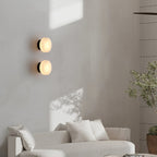 Two black-backed Clérachic Glim Round Alabaster Wall Sconces lit one above the other on a limewash wall behind a pale sofa.