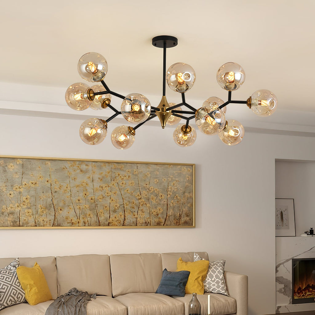 Amber glass globes glow on this Clérachic chandelier, hung above a beige sofa with yellow cushions and a gold-framed painting.