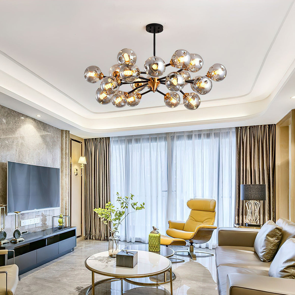 A Clérachic chandelier in a recessed ceiling lights a large living room with a yellow lounge chair and a round gold coffee table.
