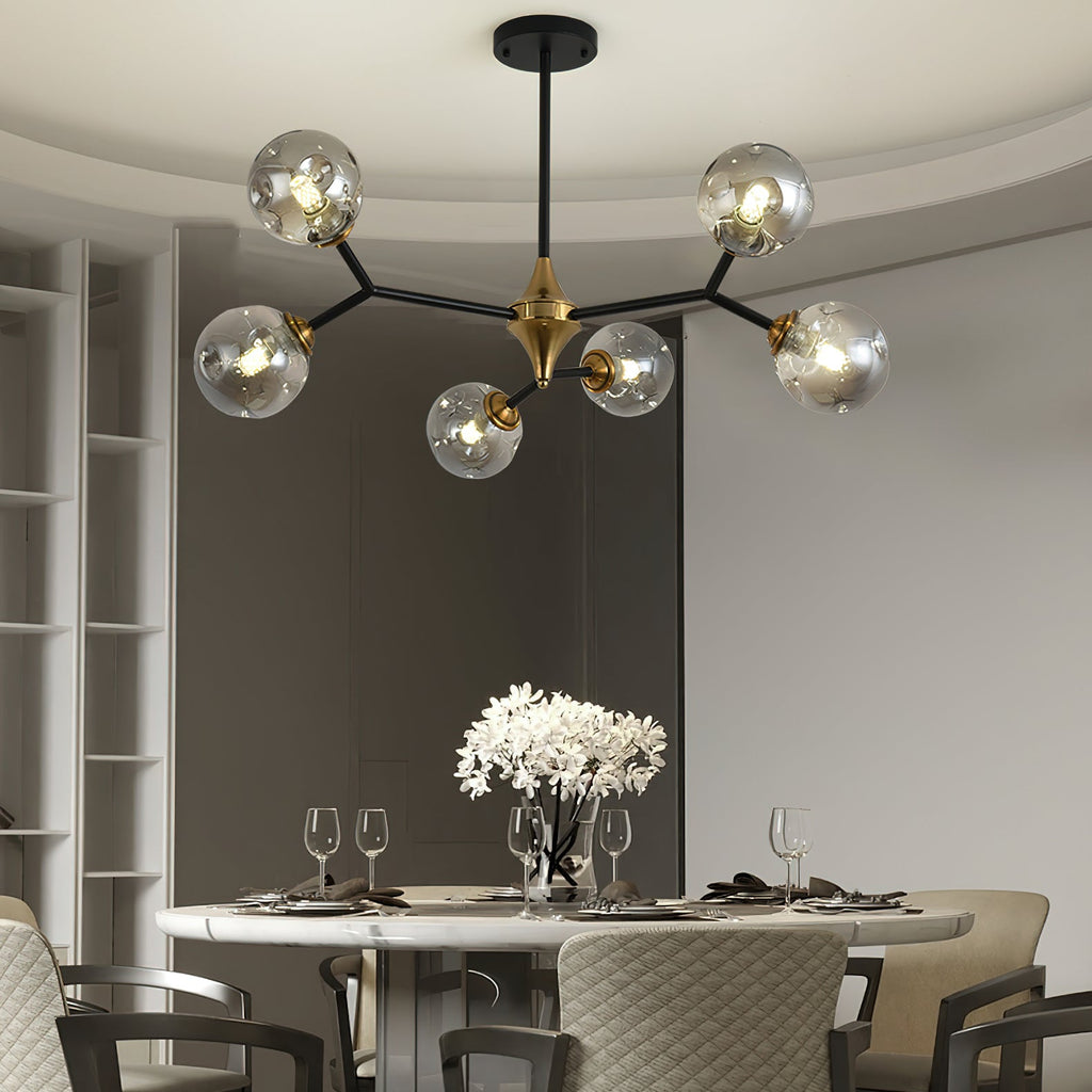 A smaller Clérachic chandelier with grey glass globes hangs over a round marble dining table set with glasses and white flowers.