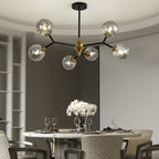 A smaller Clérachic chandelier with grey glass globes hangs over a round marble dining table set with glasses and white flowers.