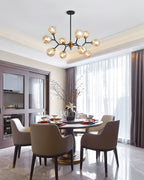 A small Clérachic chandelier with amber globes hangs in a dining room above a round table with taupe chairs and tall curtains.