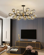 A Clérachic chandelier with smoky grey globes hangs over a living room with a wall-mounted television and a gold-edged cabinet.