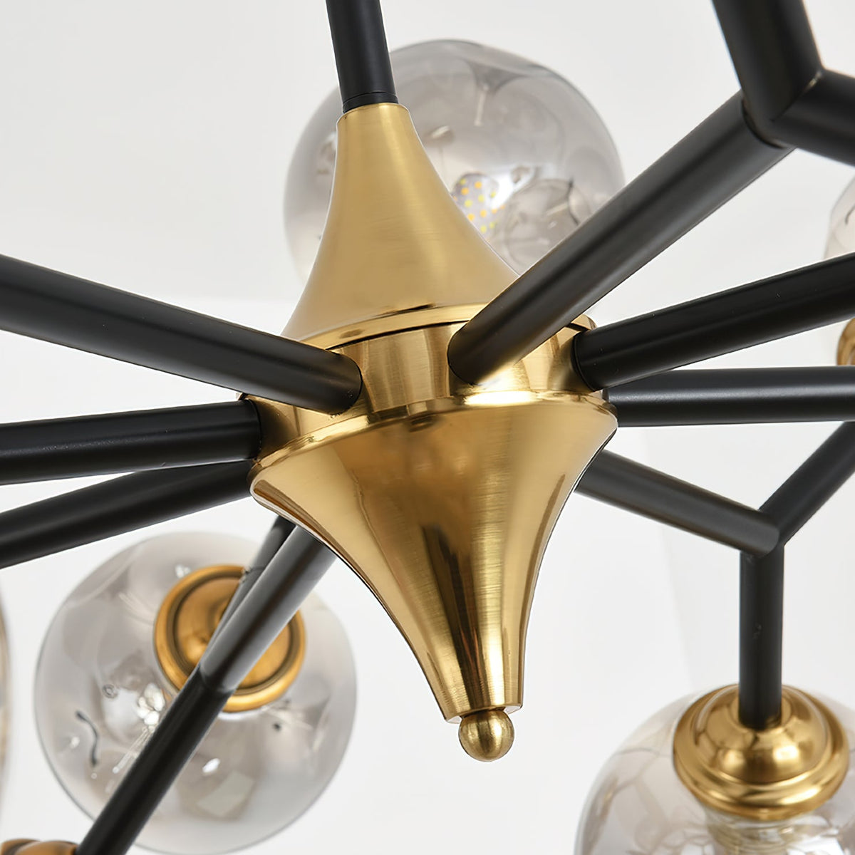Close view of the brass hub where the black arms of this Clérachic chandelier meet, with glass globes just visible behind.