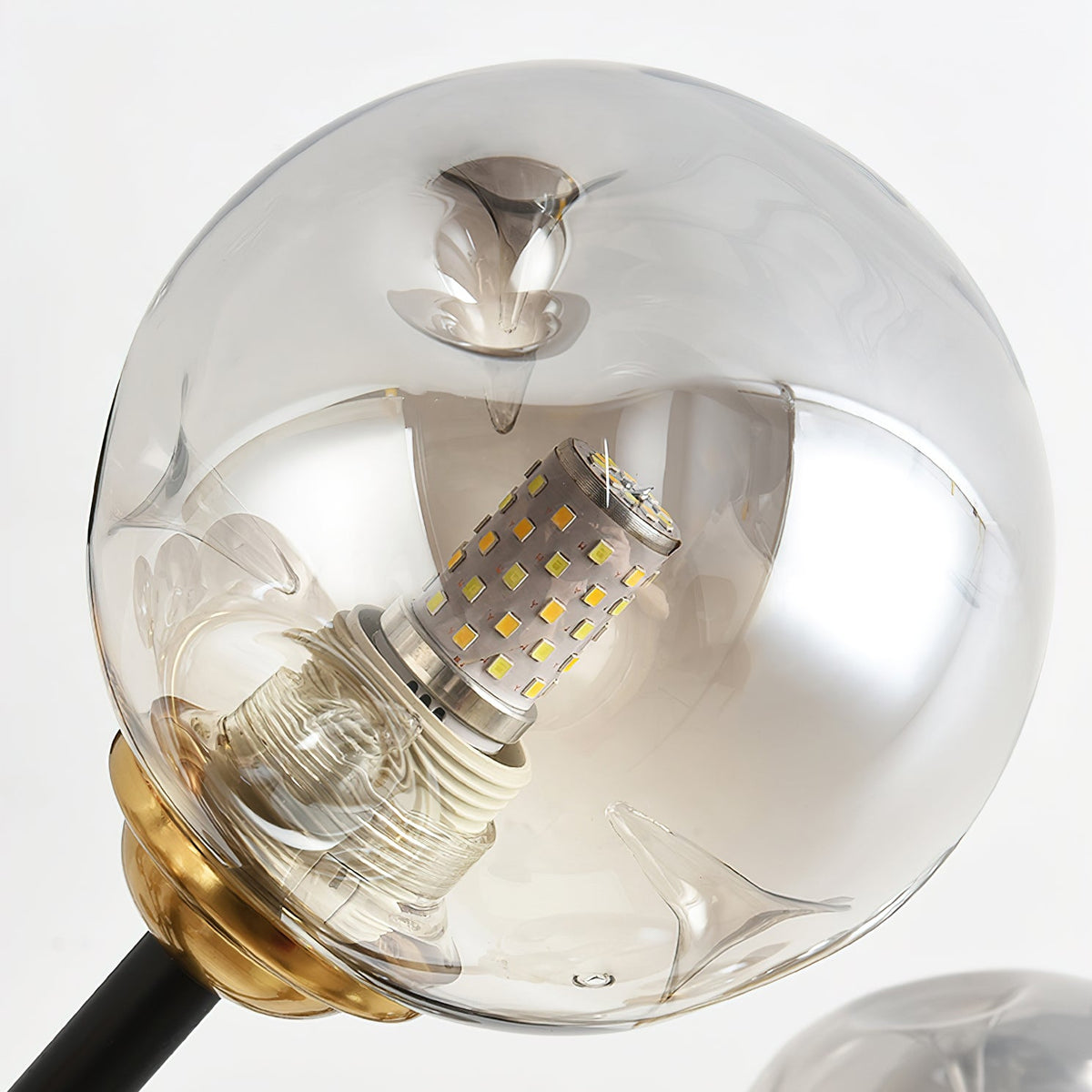 Close view of one smoky grey glass globe, with a bulb visible inside, held on a brass fitting on this Clérachic chandelier.