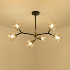 Amber Clérachic chandelier lit warm against a cream ceiling, its black arms and brass hub spreading into five arms.