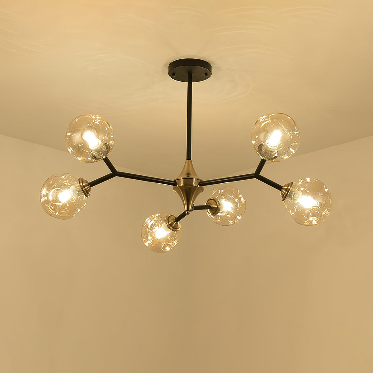 Amber Clérachic chandelier lit warm against a cream ceiling, its black arms and brass hub spreading into five arms.
