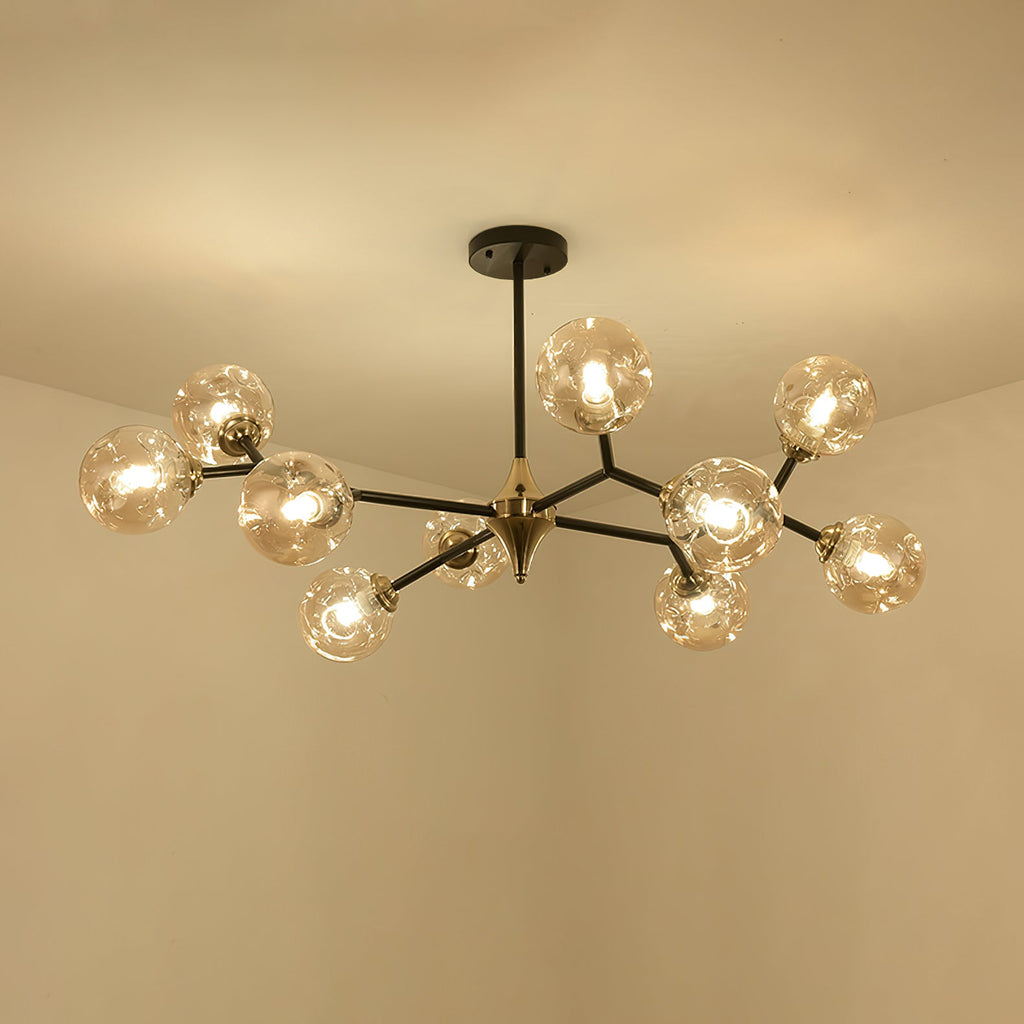 A larger amber Clérachic chandelier, lit, with black arms branching out from a brass hub against a warm cream ceiling.