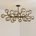 The fullest smoky grey Clérachic chandelier, lit, with clustered glass globes on black branches against a pale corner ceiling.