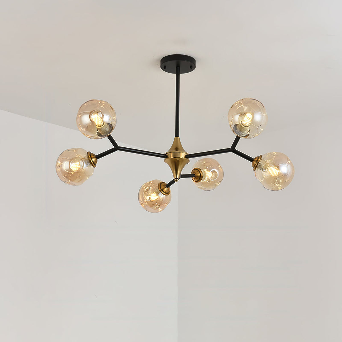 A small Clérachic chandelier with amber globes on five black arms hangs in a pale corner, a brass hub at its centre.