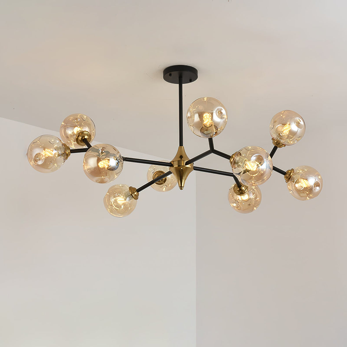 This Clérachic chandelier, lit amber, spreads black arms and round glass globes across a pale corner ceiling.