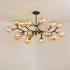 A large amber Clérachic chandelier lit warm, with globes crowded along its black branches around a brass centre.