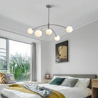 Chrome Clérachic globe chandelier above a bed in a bright bedroom with a yellow throw, green cushions and a palm outside the window.