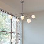 Chrome Clérachic chandelier seen against a tall window with blinds, its five frosted globes lit and the rod hanging from the ceiling.